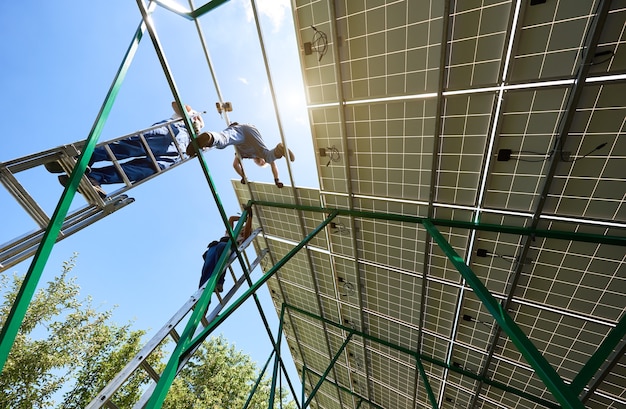 Technicians installing new, high-efficiency solar panels on a commercial building. The sky is clear and sunny.