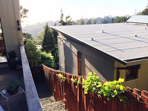 A close-up view of a solar panel installation on a residential rooftop, with a focus on the photovoltaic cells and the surrounding neighborhood.