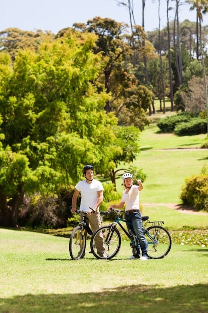 A family riding bicycles together on a sunny day in a park, with green trees and blue skies in the background.