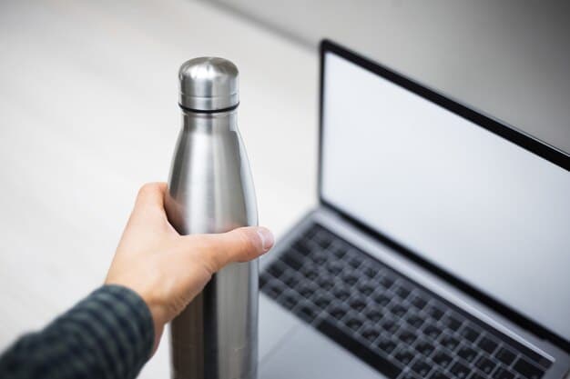 A close-up of a stainless steel water bottle with condensation, sitting on a desk next to a laptop and a plant, symbolizing sustainable hydration at work.