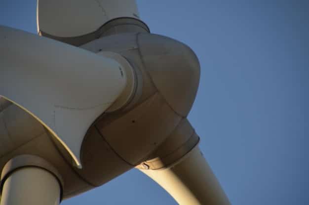 A close-up of a wind turbine blade being manufactured in a factory. Workers in protective gear are inspecting the blade, highlighting the advanced technology and precision involved in wind turbine production. The environment is clean and well-lit, showcasing the modern manufacturing processes used in the industry.