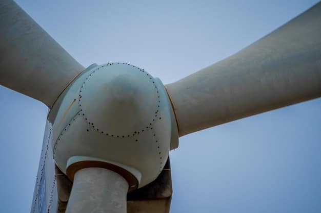 A close-up photograph of a wind turbine in a wind farm located in the American Midwest. The focus is on the enormous blades slicing through the air, with a clear sky in the background, representing clean energy production.