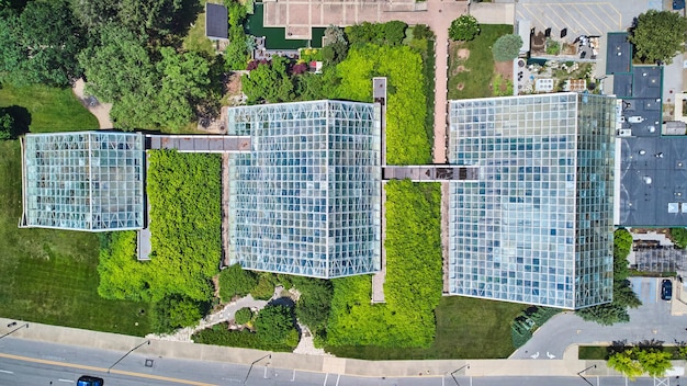 An aerial view of a modern, eco-friendly office building with a green roof and solar panels integrated into the design. The building is surrounded by lush greenery and trees.