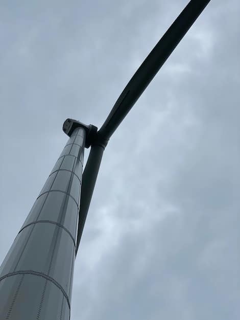 A close-up shot of the base of an exceptionally tall wind turbine. The image should emphasize the immense scale of the turbine, with the supporting structure rising dramatically into the sky. Include details of the engineering and construction.