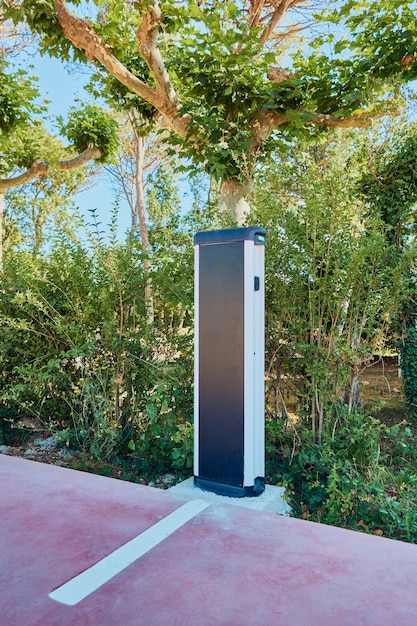 A charging station for electric vehicles in a parking lot with several EVs plugged in and charging. The background shows an urban setting with buildings and trees.