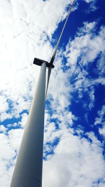 A close-up view of a wind turbine blade in motion against a bright blue sky, highlighting the engineering and mechanical aspects of wind energy technology. The image emphasizes the smooth, aerodynamic curve of the blade.