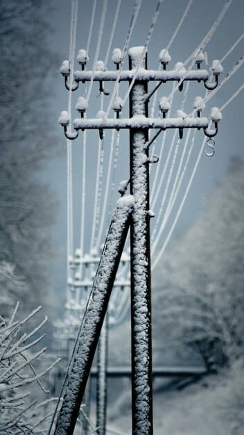 A close-up shot of a downed power transmission tower after an ice storm in the Midwest of the United States. The tower is covered in thick ice, and the surrounding landscape is blanketed in snow and ice.