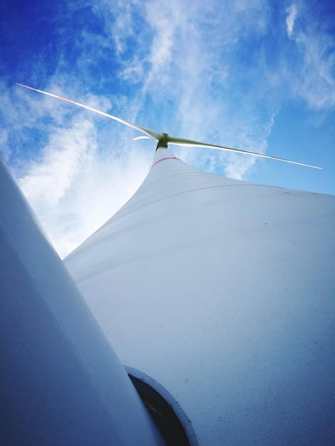 A detailed close-up of a wind turbine blade, showing its aerodynamic design and massive scale. The background is a vibrant blue sky with scattered clouds.
